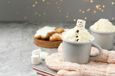 Photo of Funny snowman made with marshmallow and whipped cream in cup of hot drink served on grey background against Christmas lights