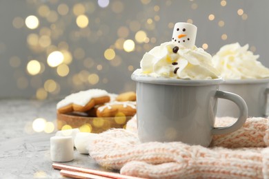 Photo of Funny snowman made with marshmallow and whipped cream in cup of hot drink served on grey background against Christmas lights, closeup. Space for text