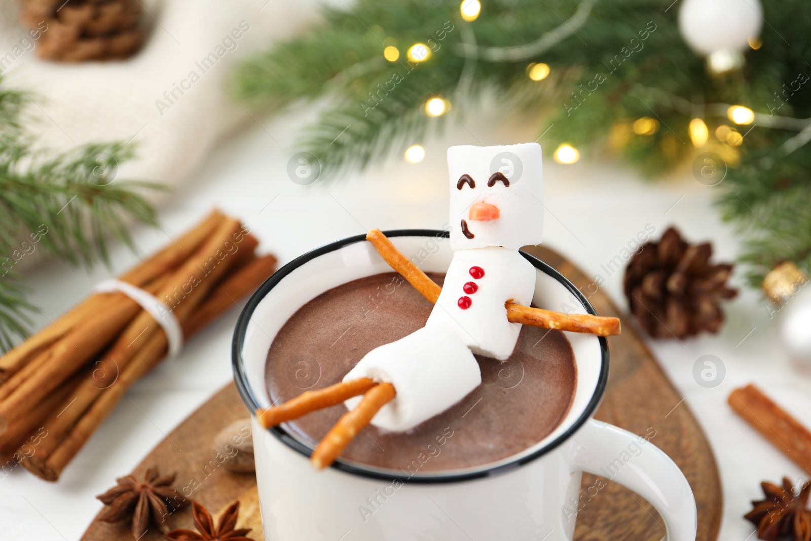 Photo of Funny snowman made with marshmallows in cup of hot chocolate and winter decor on white table, closeup