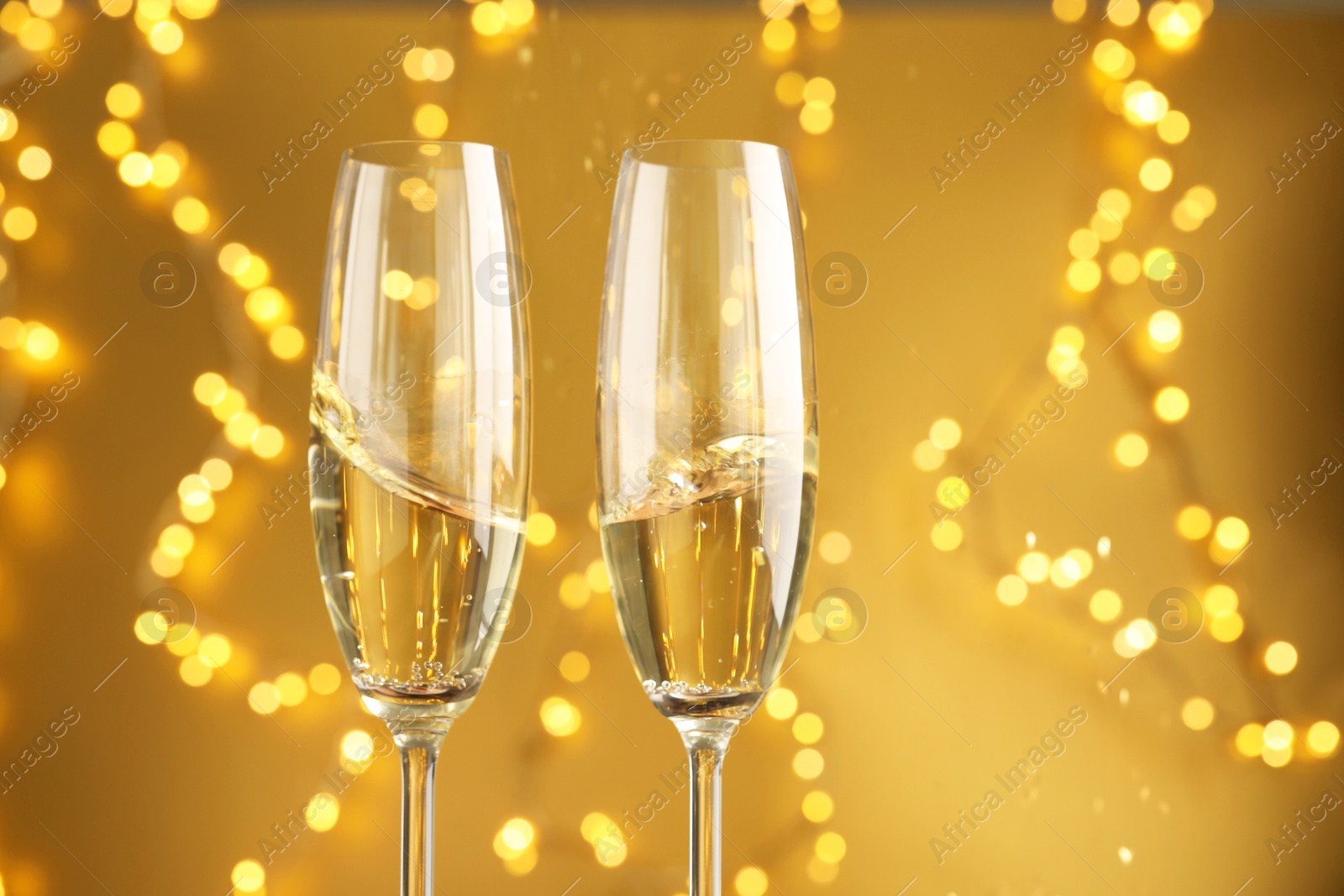 Photo of Glasses of sparkling wine against golden background with blurred lights, closeup. Christmas decor