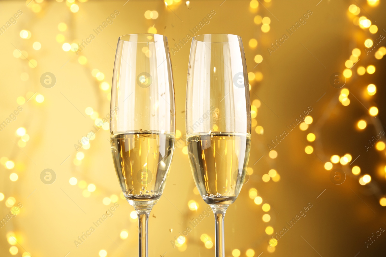 Photo of Glasses of sparkling wine against golden background with blurred lights, closeup. Christmas decor