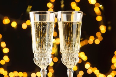 Photo of Glasses of sparkling wine and confetti against dark background with blurred lights, closeup. Christmas decor