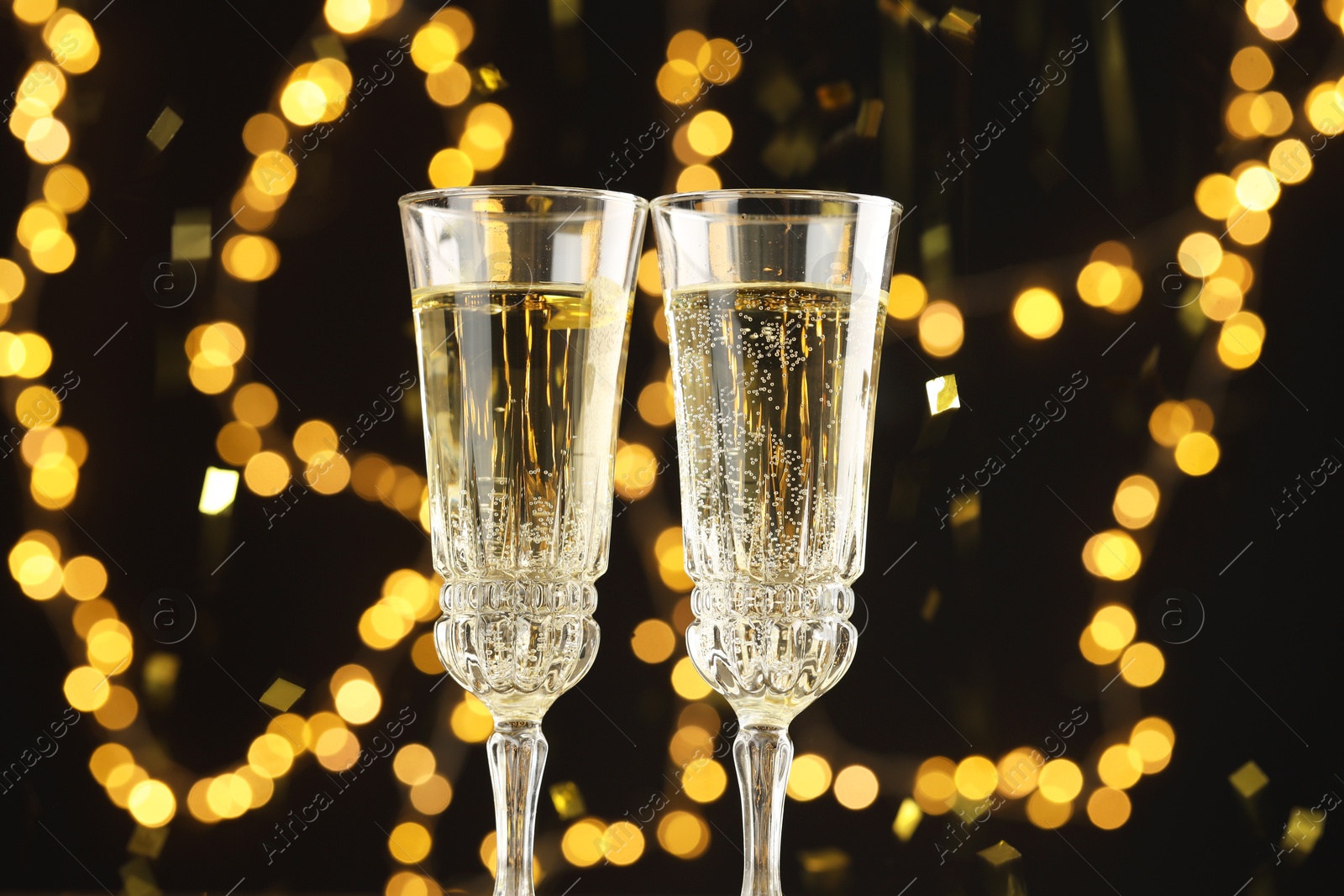 Photo of Glasses of sparkling wine and confetti against dark background with blurred lights, closeup. Christmas decor