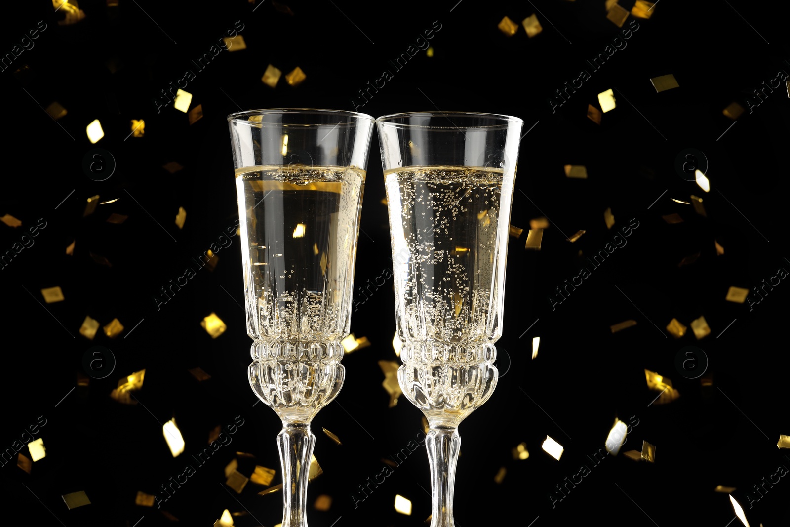 Photo of Glasses of sparkling wine and confetti against dark background, closeup. Christmas decor