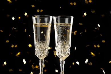 Photo of Glasses of sparkling wine and confetti against dark background, closeup. Christmas decor