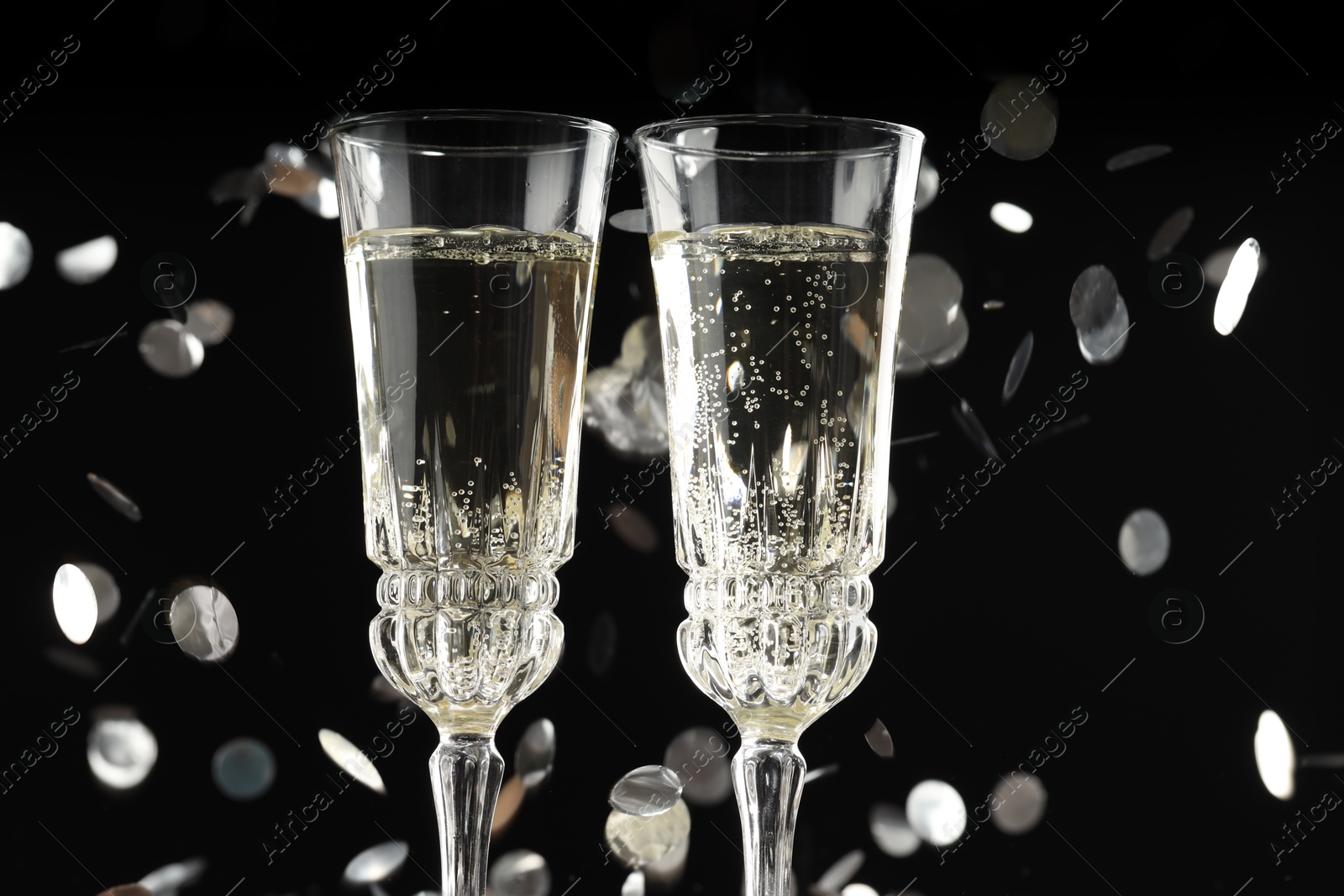 Photo of Glasses of sparkling wine and confetti against dark background, closeup. Christmas decor