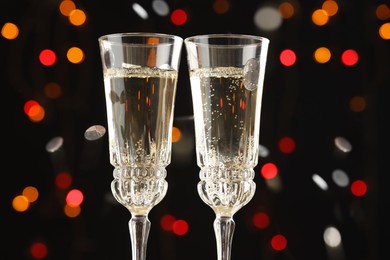 Photo of Glasses of sparkling wine and confetti against dark background with blurred lights, closeup. Christmas decor