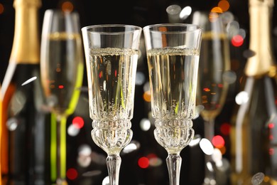 Photo of Glasses of sparkling wine and confetti against dark background with blurred lights, closeup. Christmas decor