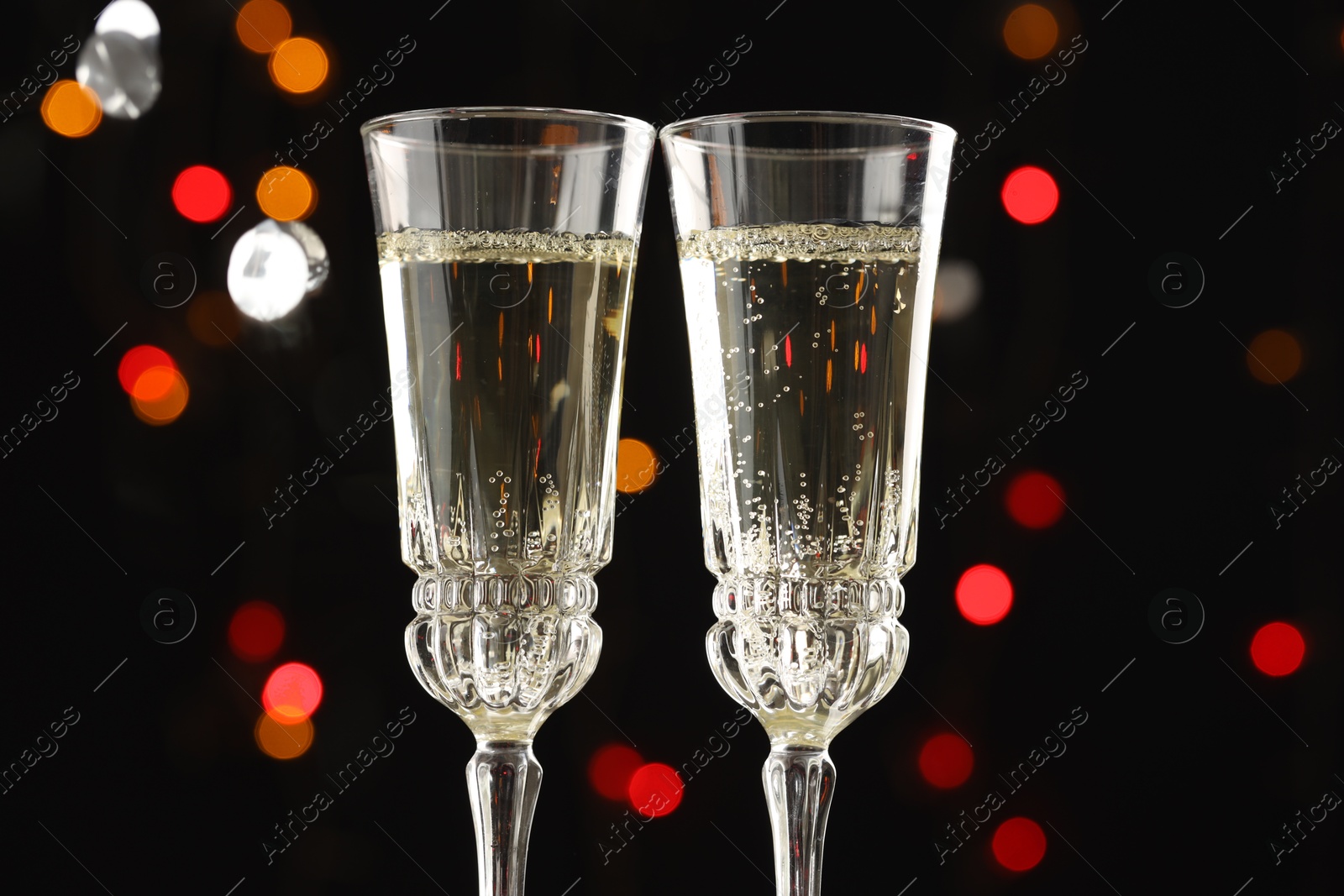 Photo of Glasses of sparkling wine and confetti against dark background with blurred lights, closeup. Christmas decor