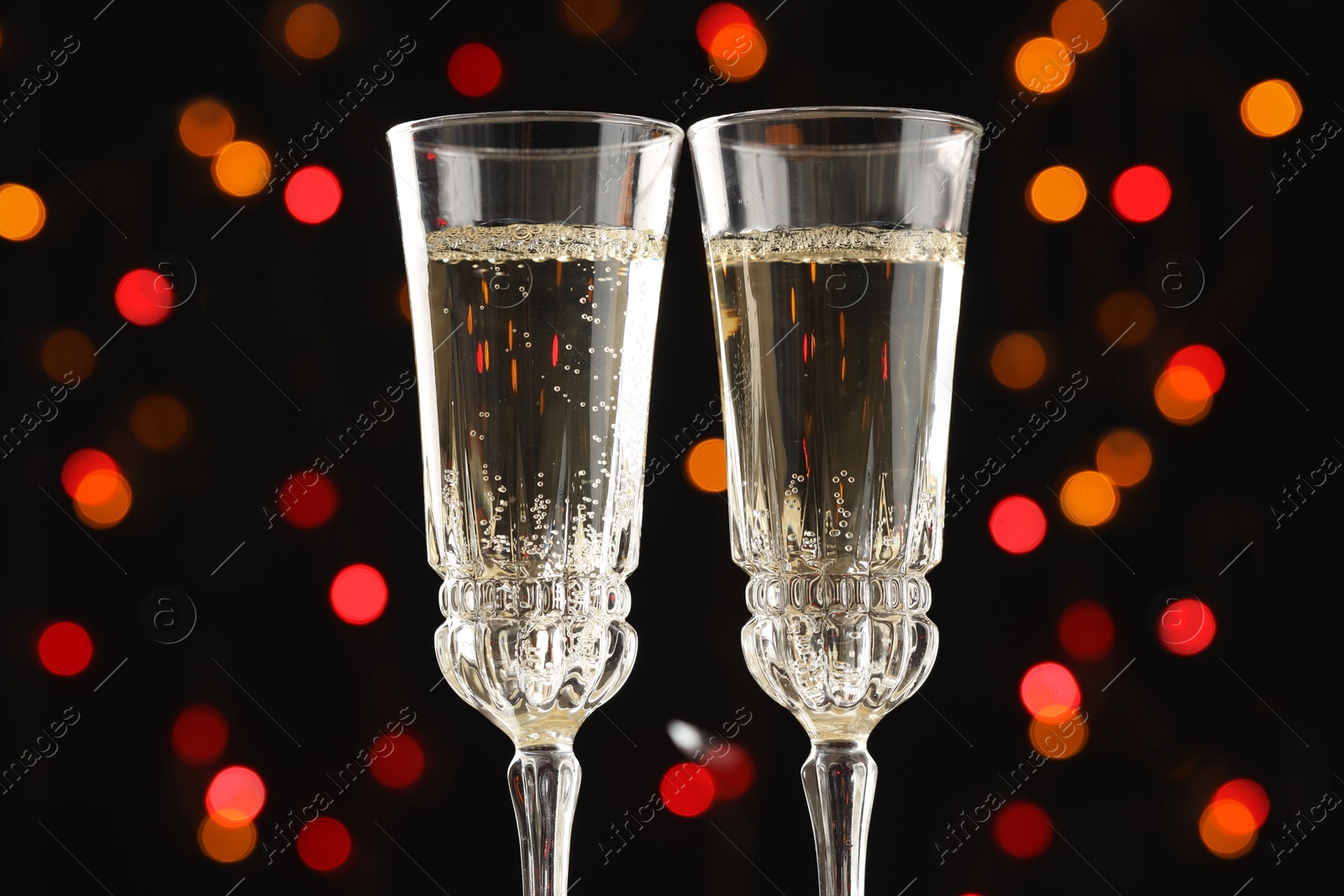 Photo of Glasses of sparkling wine and confetti against dark background with blurred lights, closeup. Christmas decor