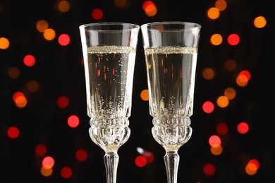 Photo of Glasses of sparkling wine and confetti against dark background with blurred lights, closeup. Christmas decor