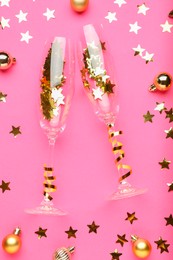 Photo of Wine glasses with confetti and Christmas balls on pink background, flat lay