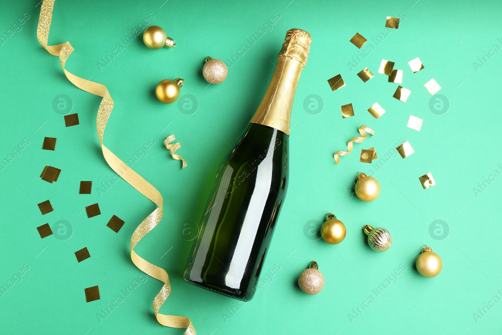 Photo of Bottle of sparkling wine, confetti and Christmas balls on green background, flat lay