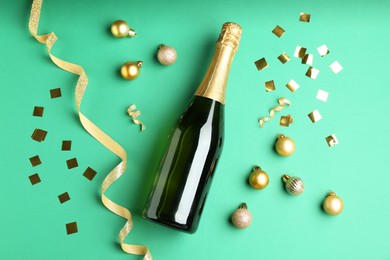 Photo of Bottle of sparkling wine, confetti and Christmas balls on green background, flat lay