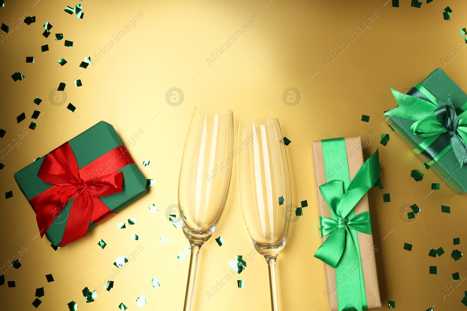 Photo of Confetti, glasses and gift boxes on golden background, flat lay with space for text. Christmas decor