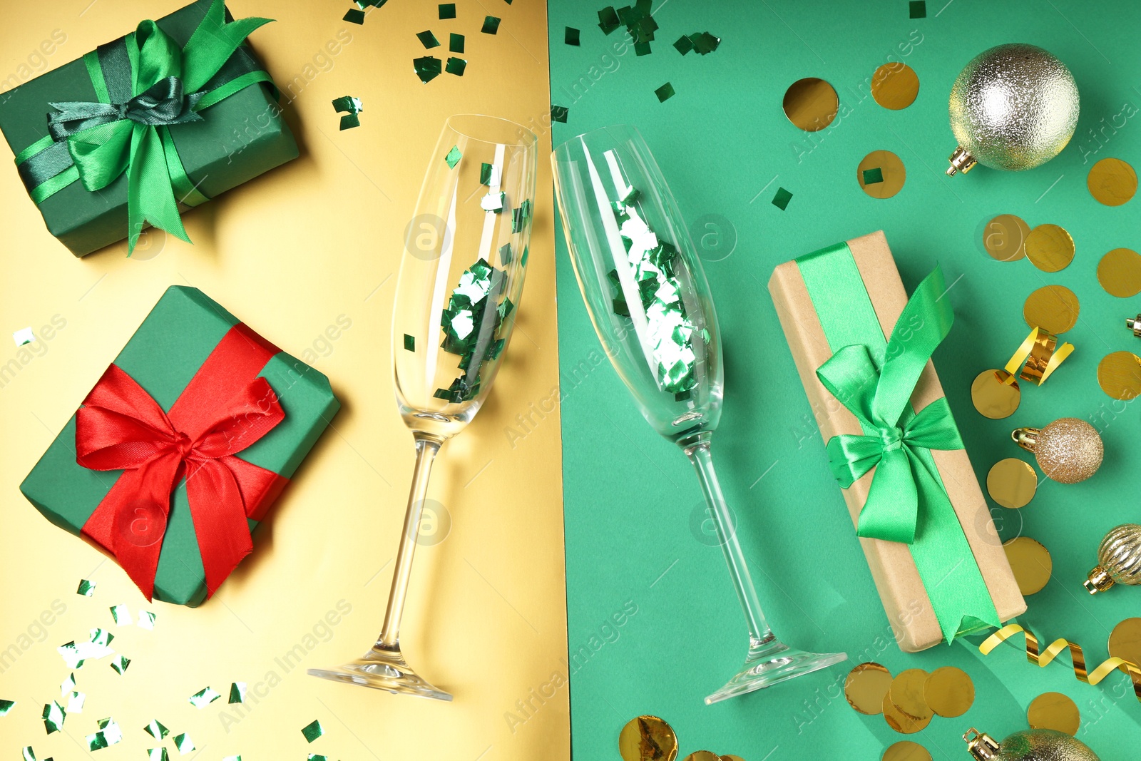 Photo of Glasses with confetti, gift boxes and Christmas balls on color background, flat lay