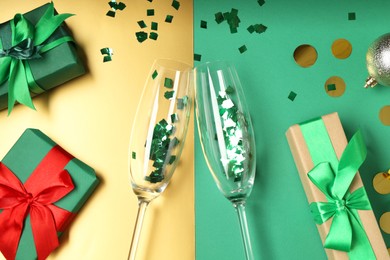 Photo of Glasses with confetti and gift boxes on color background, flat lay. Christmas decor