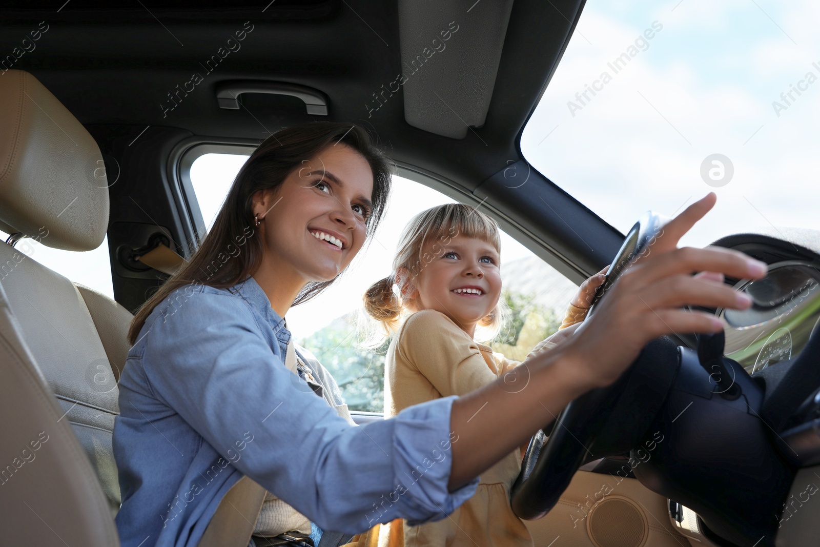 Photo of Happy woman with her daughter holding steering wheel inside car, low angle view