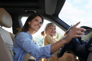 Photo of Happy woman with her daughter holding steering wheel inside car, low angle view