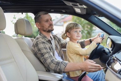 Photo of Man with his daughter holding steering wheel inside car