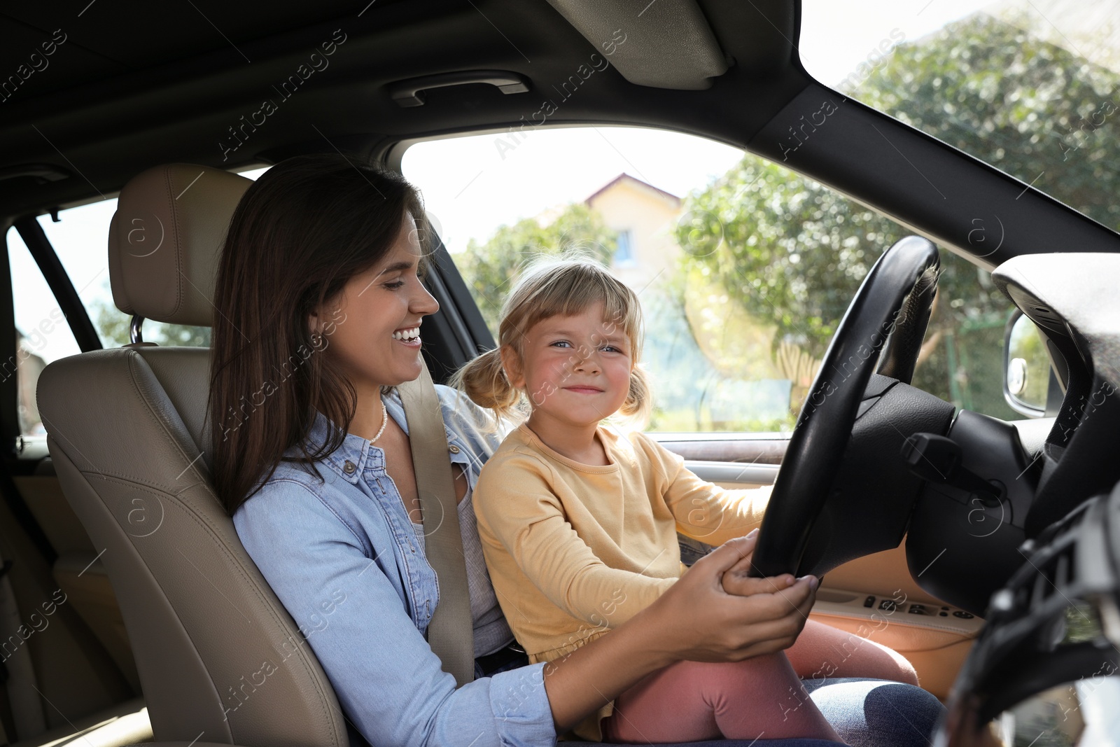 Photo of Happy woman with her daughter holding steering wheel inside car