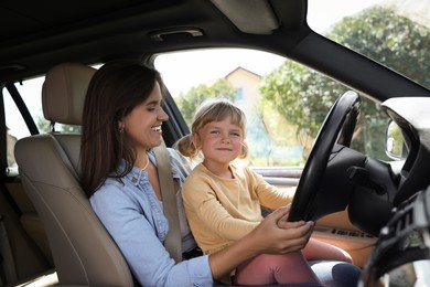 Happy woman with her daughter holding steering wheel inside car