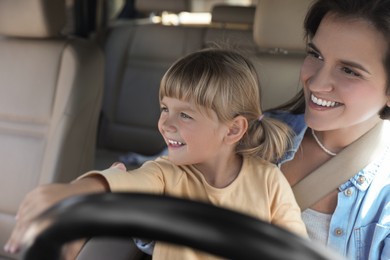 Photo of Happy woman with her daughter holding steering wheel inside car