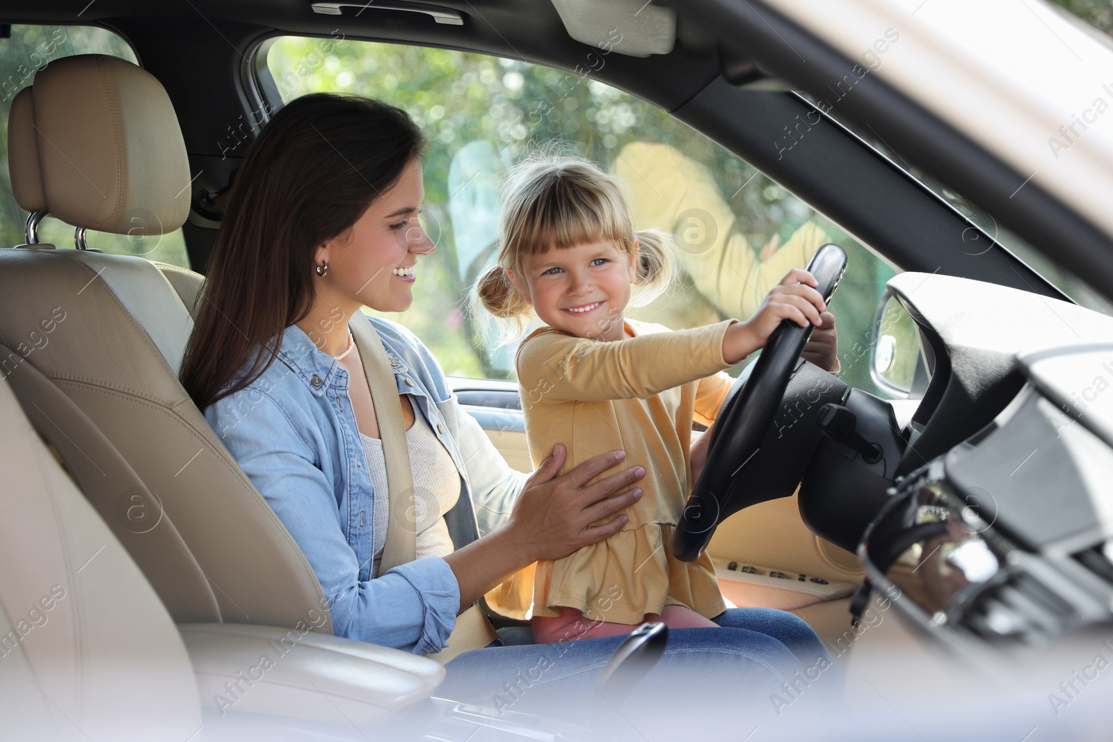 Photo of Happy woman with her daughter holding steering wheel inside car