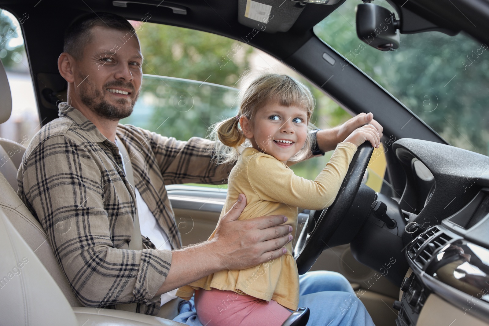 Photo of Man with his daughter holding steering wheel inside car