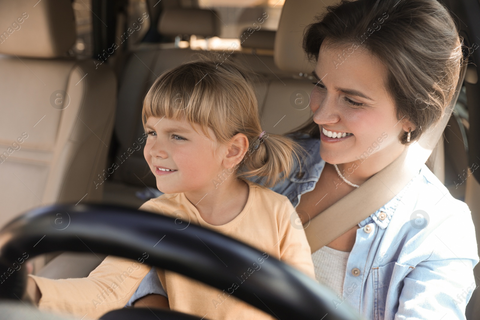 Photo of Happy woman with her daughter holding steering wheel inside car