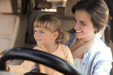 Photo of Happy woman with her daughter holding steering wheel inside car