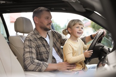 Man with his daughter holding steering wheel inside car