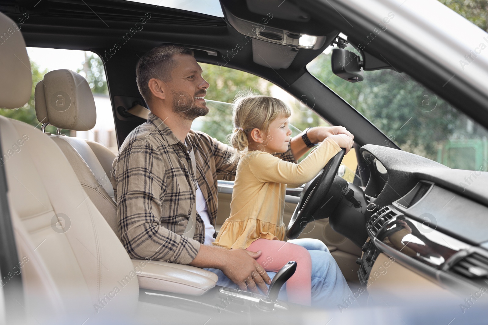 Photo of Man with his daughter holding steering wheel inside car