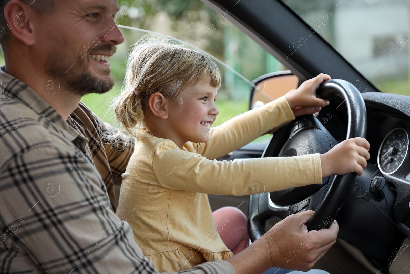 Photo of Happy man with his daughter holding steering wheel inside car