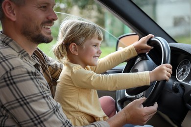 Happy man with his daughter holding steering wheel inside car