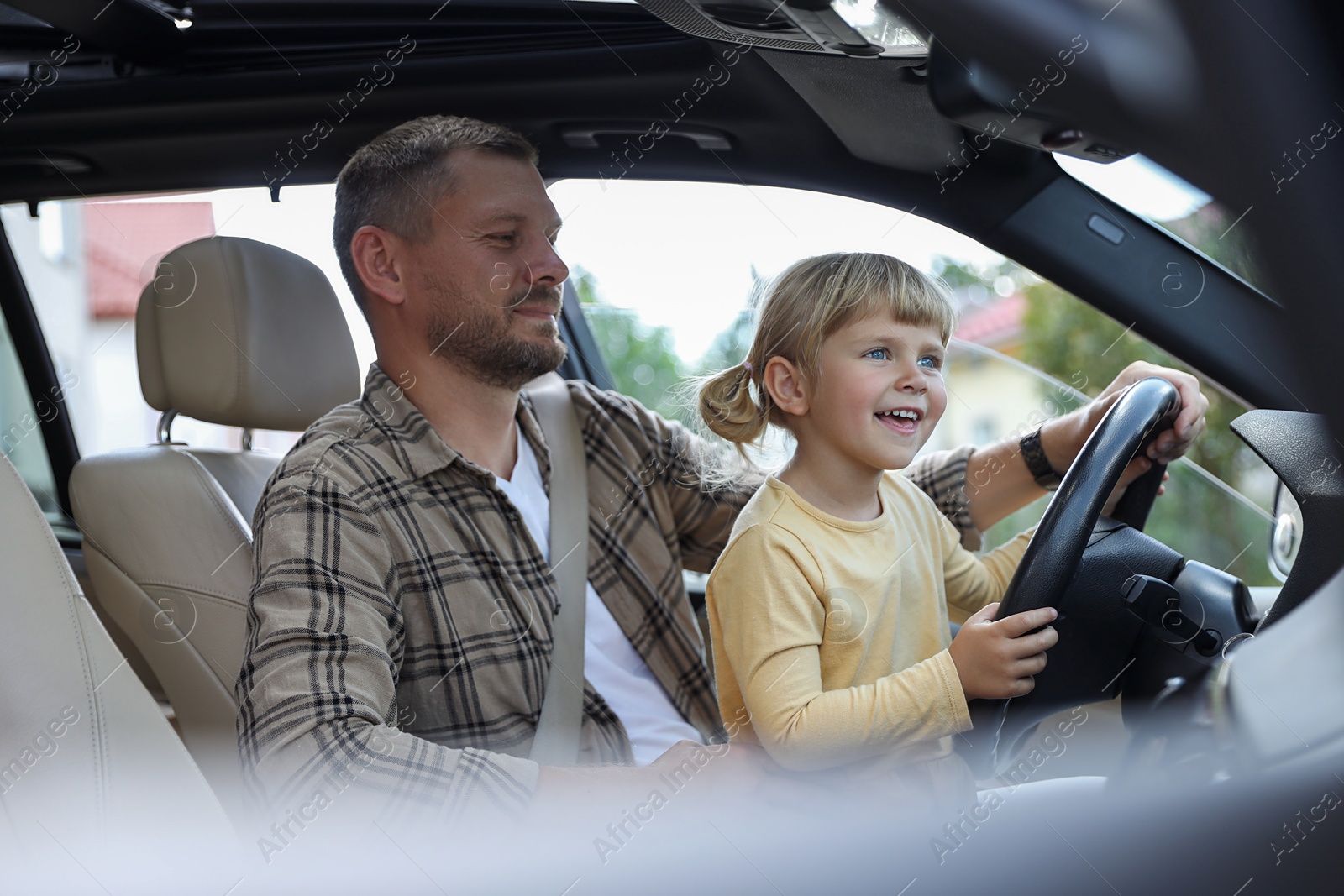 Photo of Man with his daughter holding steering wheel inside car