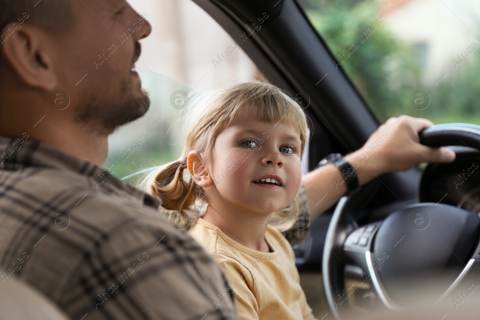 Photo of Man with his daughter holding steering wheel inside car, closeup