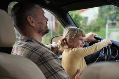 Photo of Man with daughter holding steering wheel inside car