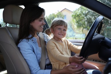 Happy woman with her daughter holding steering wheel inside car