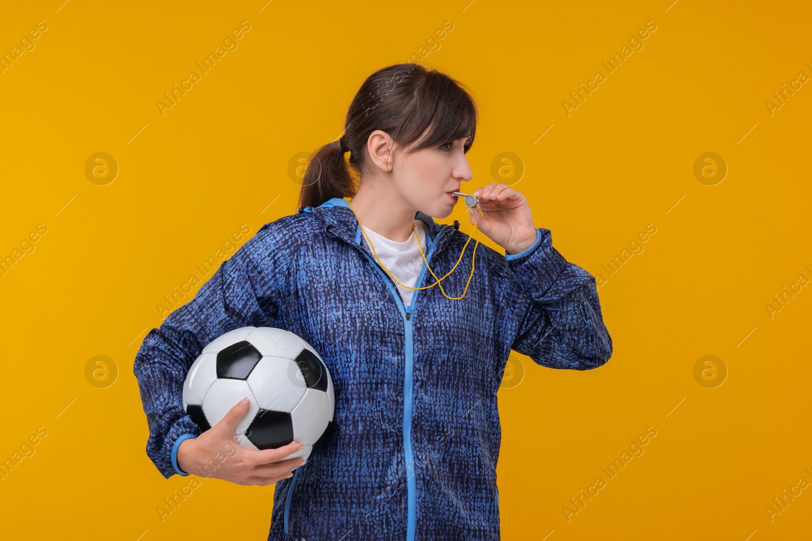 Photo of Woman with soccer ball blowing whistle on orange background