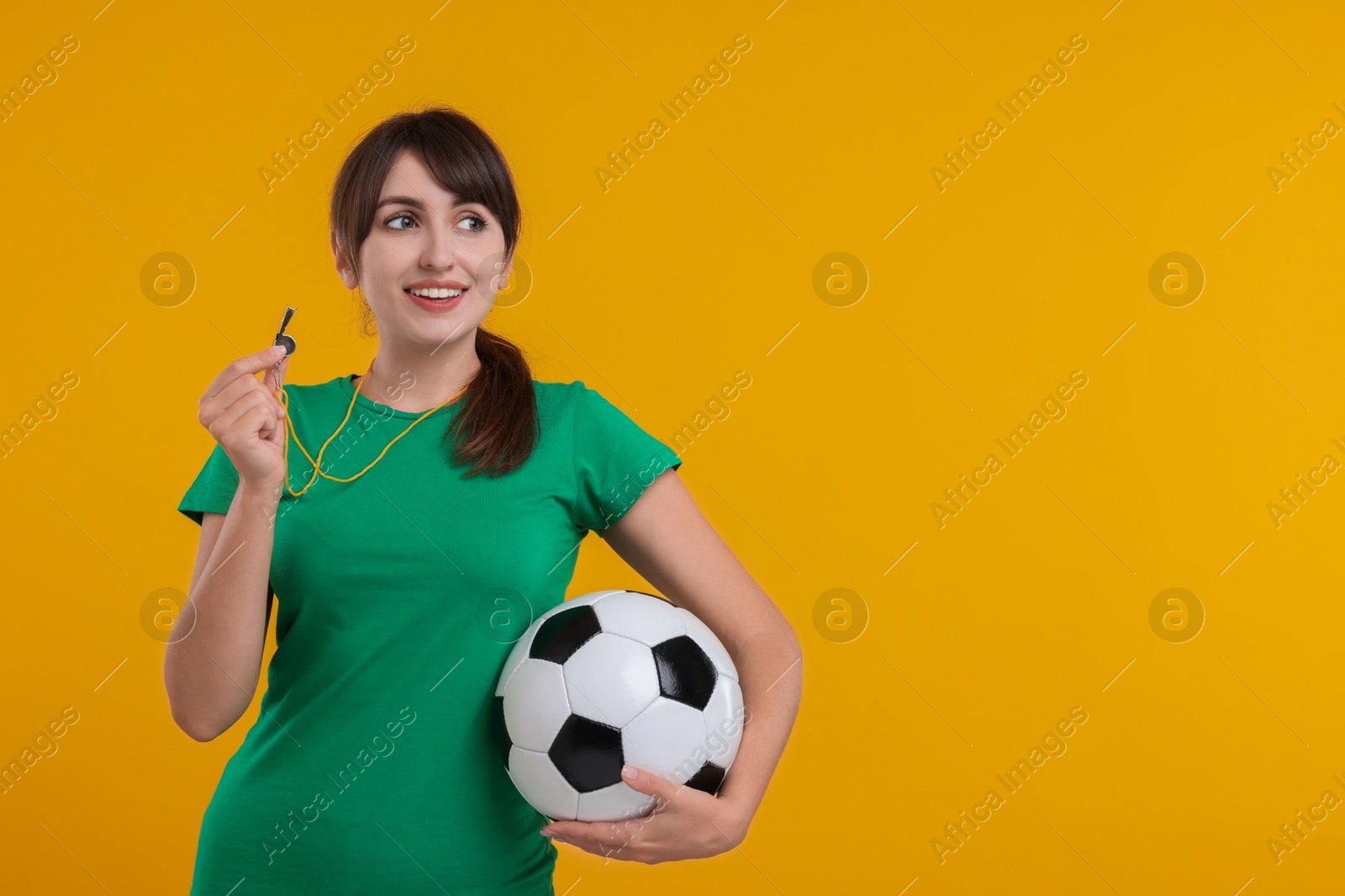 Photo of Happy woman with whistle and soccer ball on orange background, space for text