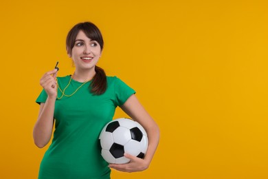 Photo of Happy woman with whistle and soccer ball on orange background, space for text