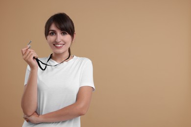 Happy woman with whistle on beige background, space for text