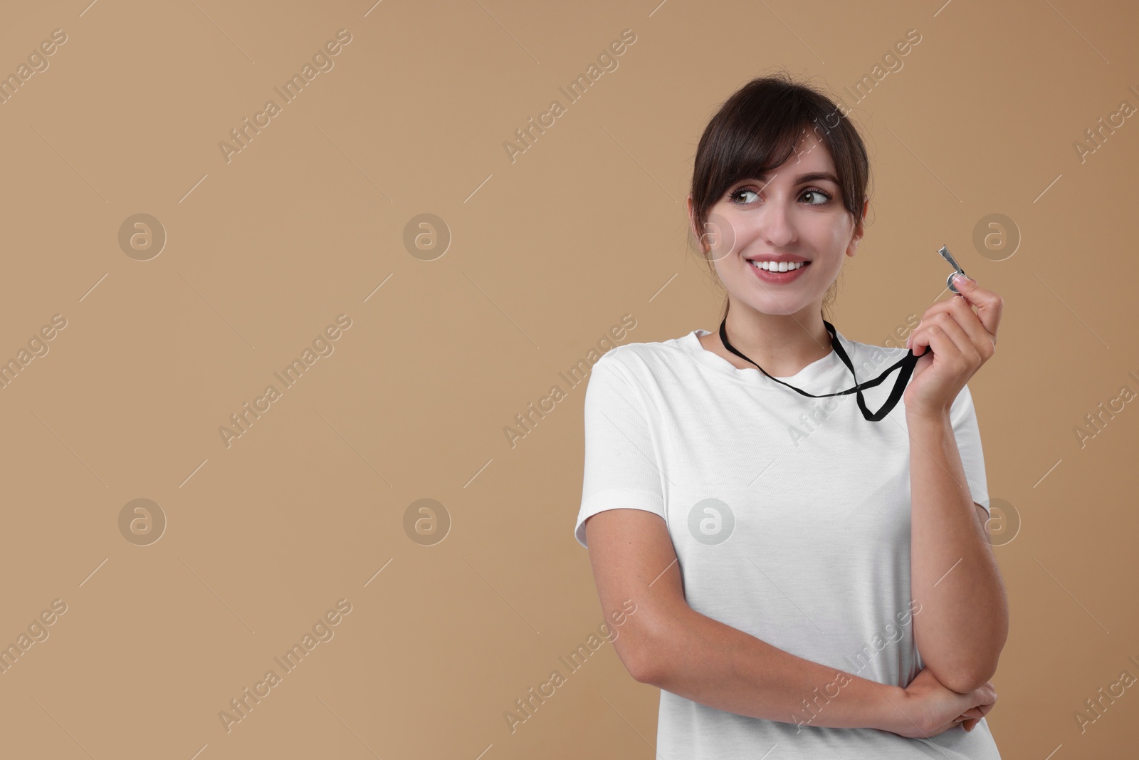 Photo of Happy woman with whistle on beige background, space for text