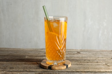 Glass of tasty refreshing drink and straw on wooden table against gray background