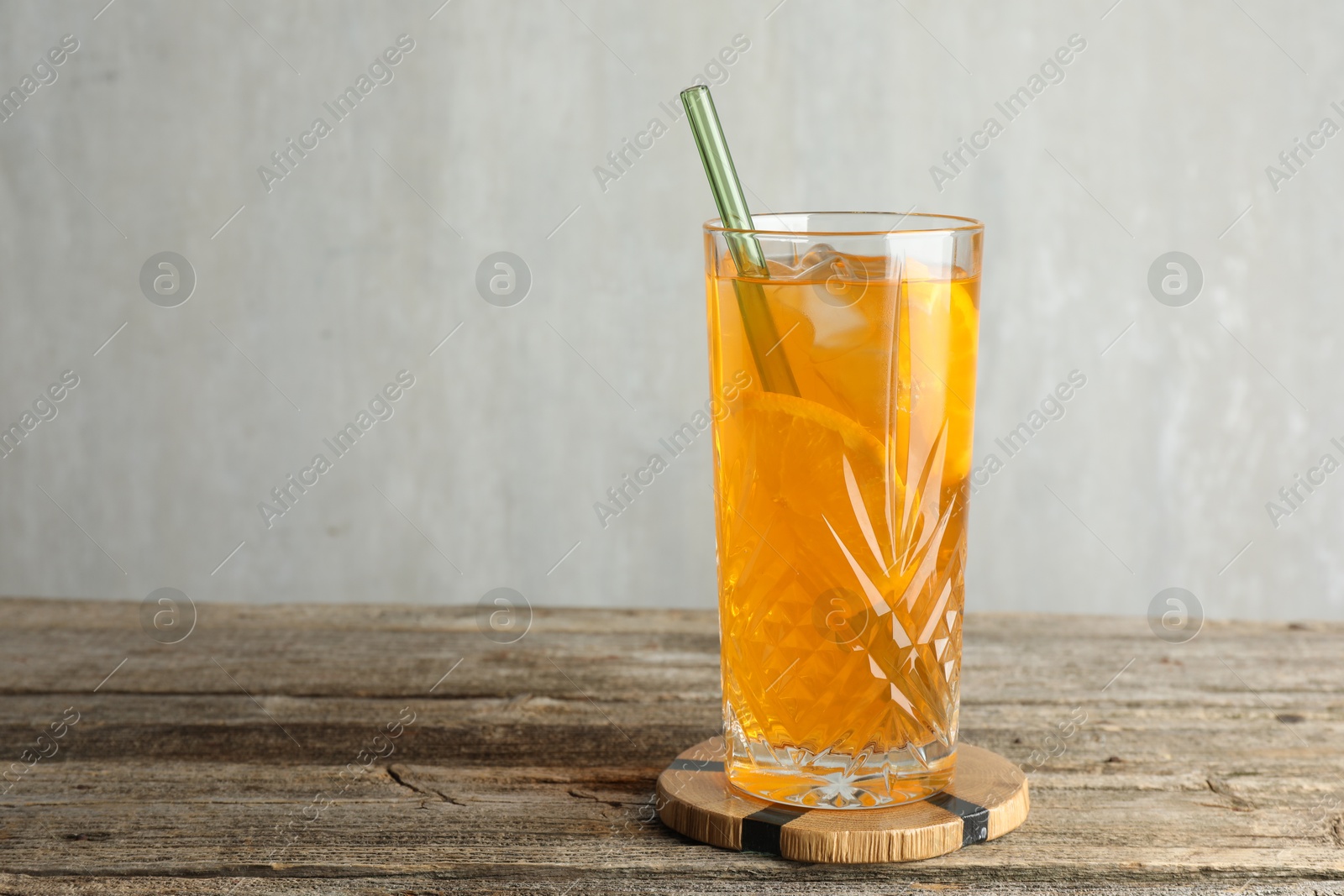 Photo of Glass of tasty refreshing drink and straw on wooden table against gray background