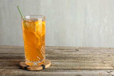 Photo of Glass of tasty refreshing drink and straw on wooden table against gray background, space for text