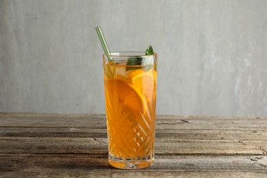 Photo of Glass of tasty refreshing drink and straw on wooden table against gray background