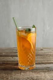 Photo of Glass of tasty refreshing drink and straw on wooden table against gray background