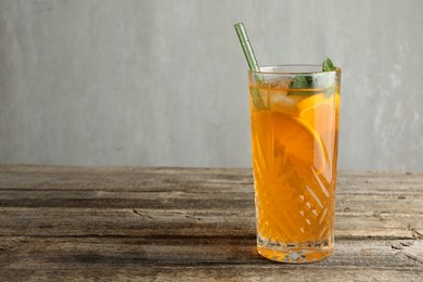 Glass of tasty refreshing drink and straw on wooden table against gray background, space for text